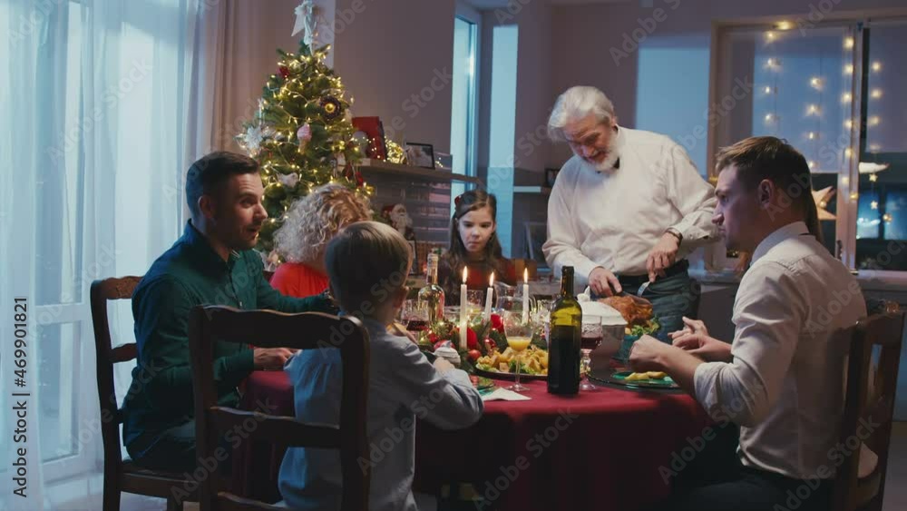 Happy caucasian family celebrating Christmas, chatting at dinner party table at home. Grandfather cuts roasted turkey while everyone is watching. Happy caucasian family celebrating Christmas, chatting at dinner party table at home. Grandfather cuts roasted turkey while everyone is watching.