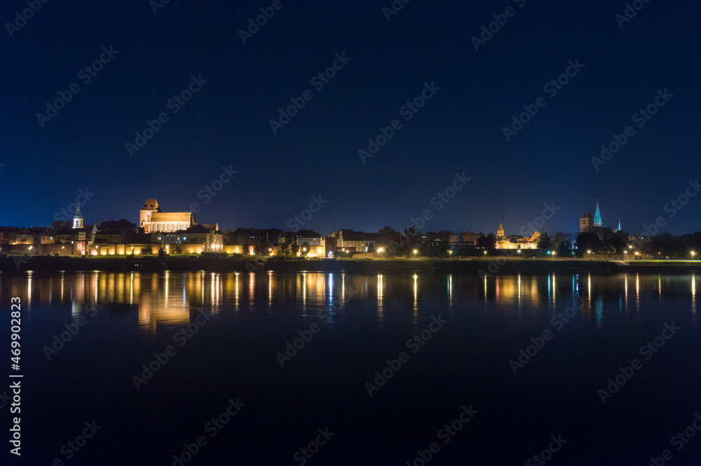 Night view of panoramic view on Old town of Torun city walls and reflection in Vistula river.