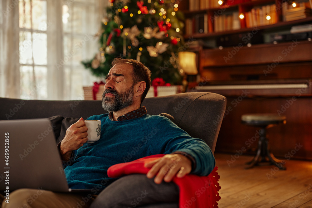 Middle age man enjoying Christmastime at home and using laptop