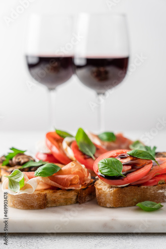 Bruschetta set with prosciutto and basil, tomatoes and mozzarella, camembert and berries, mushrooms and parsley on marble board. Antipasto open sandwich appetizer