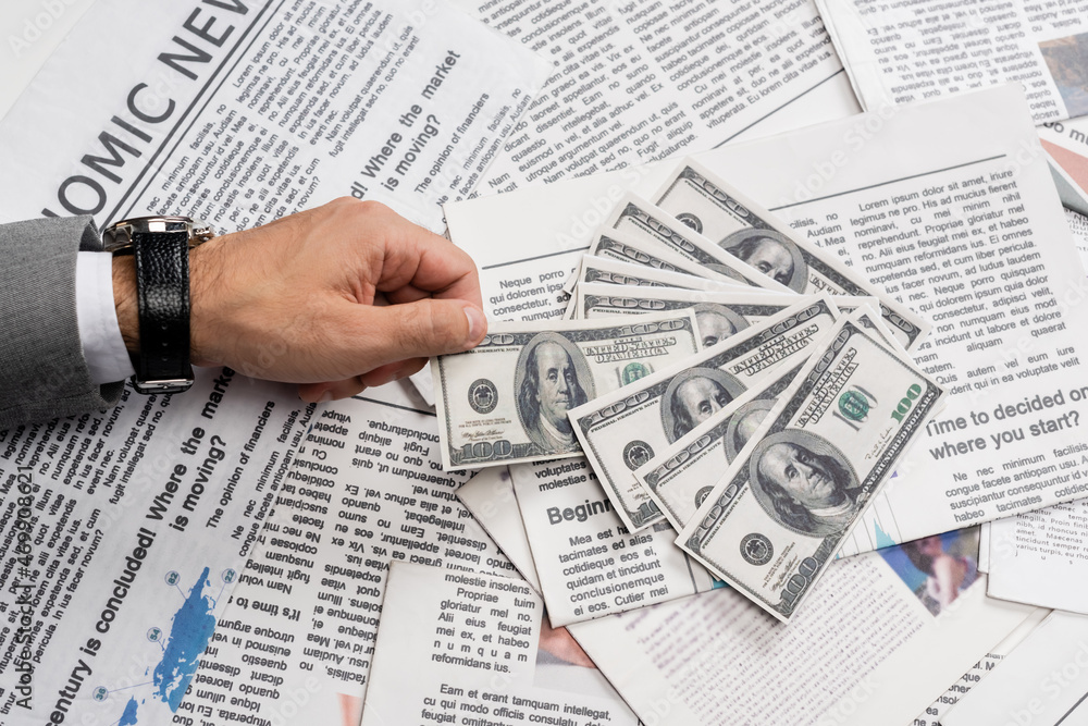 Fototapeta premium KYIV, UKRAINE - NOVEMBER 1, 2021: cropped view of man holding dollar banknote near printed newspapers