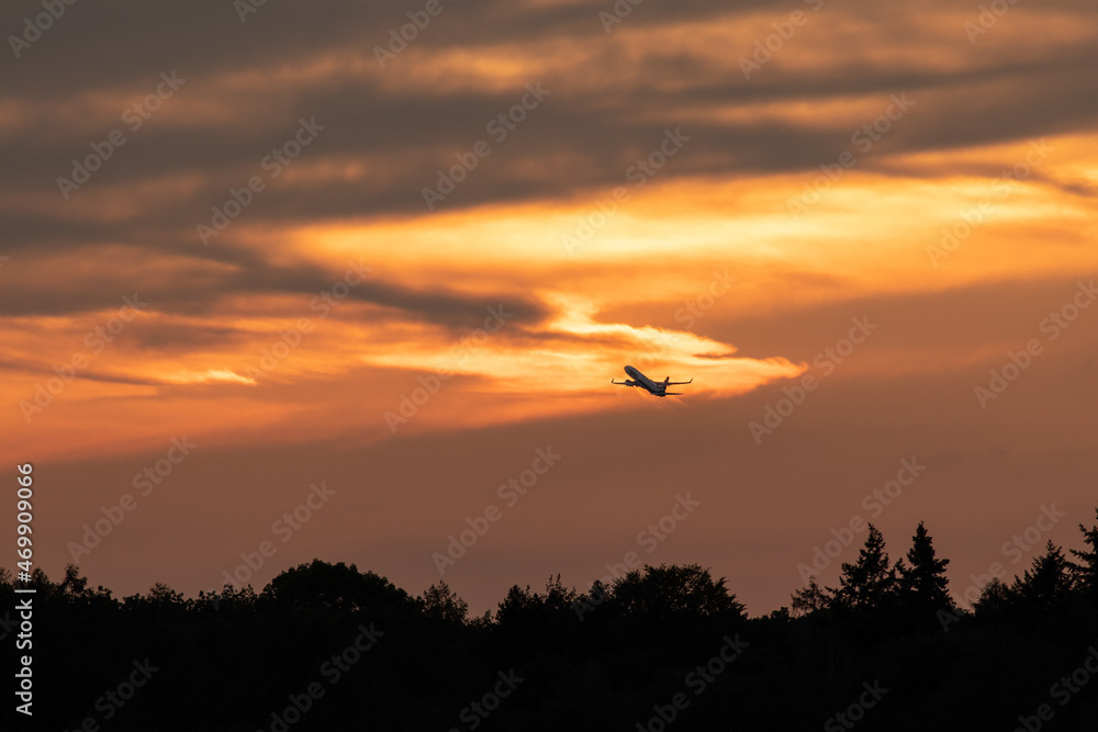 Leaving on a jetliner. Passenger plane leaving into setting sun skies. Orange colored clouds and silhouette of the plane over horizon. Travel, vacation, holiday, adventure. Let's go!