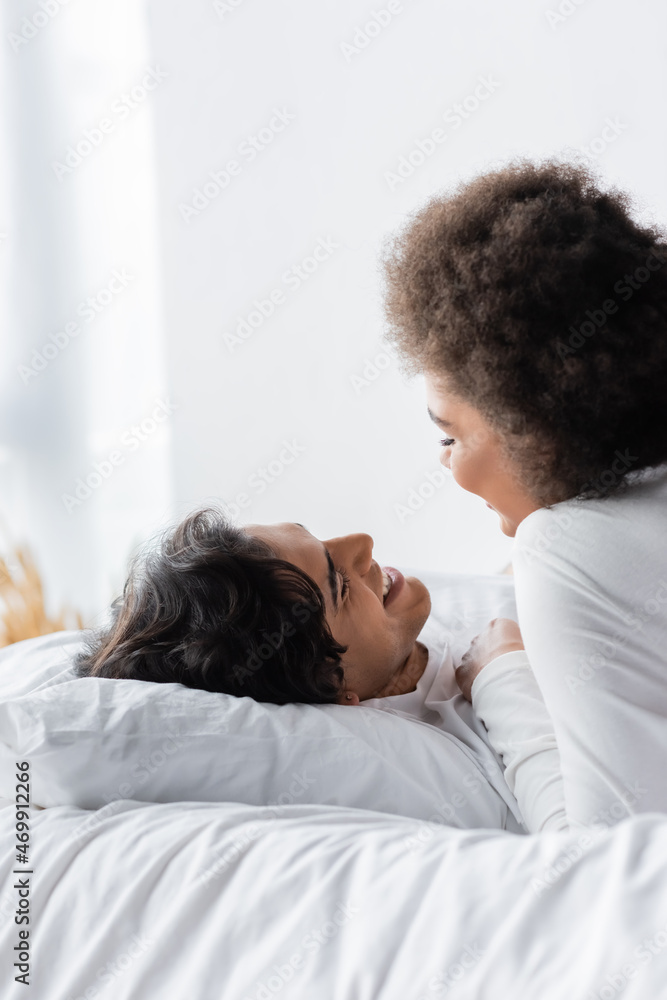 positive interracial couple smiling while looking at each other in bedroom positive interracial couple smiling while looking at each other in bedroom