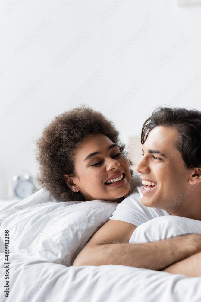 cheerful interracial couple smiling while lying on bed