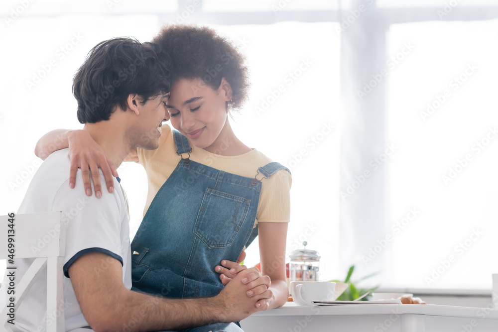 happy multiethnic couple hugging and holding hands during breakfast