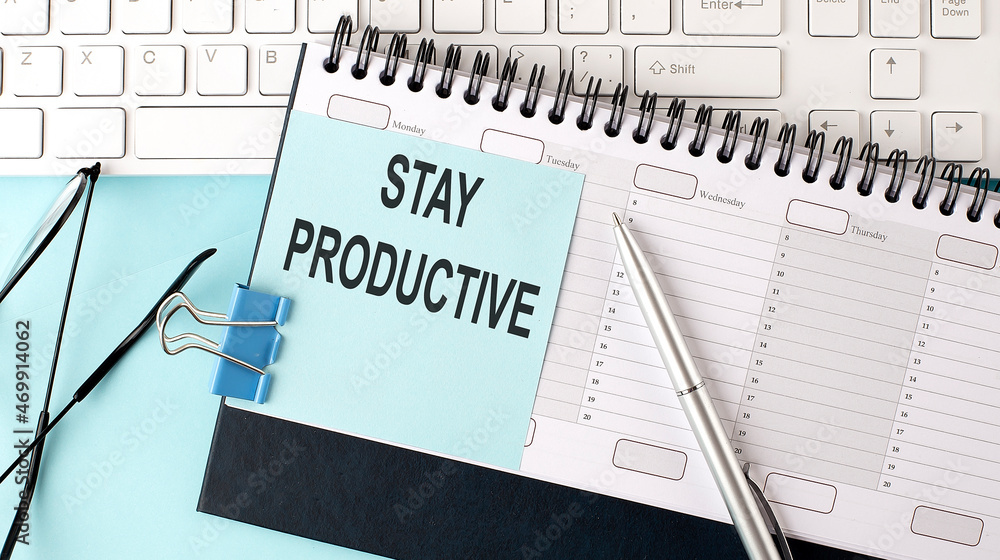 STAY PRODUCTIVE text on blue sticker on planning and keyboard,blue background STAY PRODUCTIVE text on blue sticker on planning and keyboard,blue background