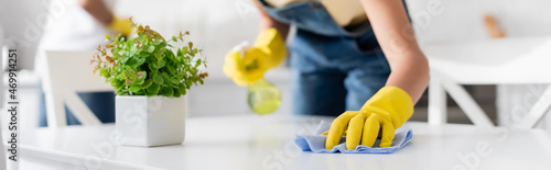 Canvastavla cropped view of african american woman cleaning dining table with rag near blurr