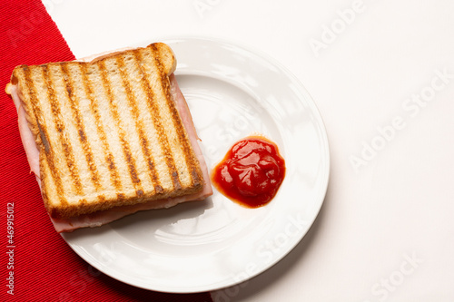 Ham cheese toast with ketchup on a white plate with a white and red background