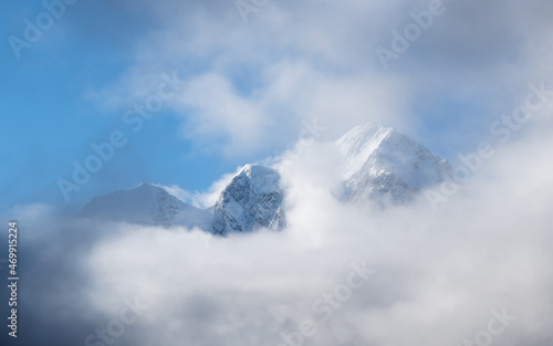 Panoramic alpine sunny landscape with high snowy mountain with peaked top and glacier above low clouds. Big snow covered mountains in sunshine. White-snow pointy peak in sunlight.