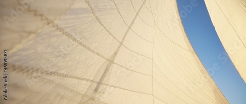 Fotografie White sails of a sloop rigged yacht against clear blue sky with plane tracks at sunset