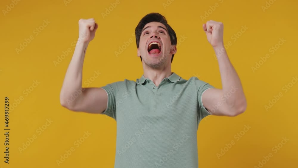 Excited jubilant overjoyed happy joyful attractive happy young man 20s years old wears blue t-shirt doing winner gesture celebrate clenching fists say yes isolated on plain yellow background studio Excited jubilant overjoyed happy joyful attractive happy young man 20s years old wears blue t-shirt doing winner gesture celebrate clenching fists say yes isolated on plain yellow background studio