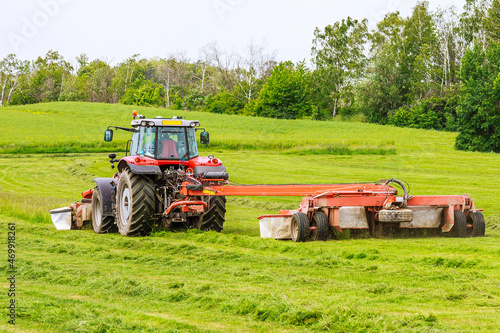 A tractor with two rotary mowers mows the grass. Mowers in front and behind the tractor