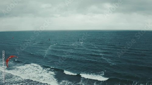 Aerial view of the kite surfers surfing in high winds in the rough sea. The foam is on the sea. Kite surfing video.