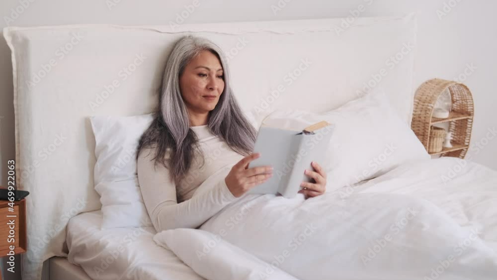 Handsome Asian woman reading a book and looking at the phone in the bed Handsome Asian woman reading a book and looking at the phone in the bed