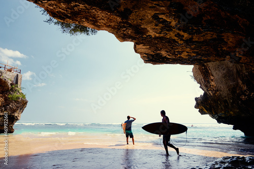 Hobby and vacation. Surfers with surfboard on beautiful beach with high rocks. Uluwatu spot, Bali island, Indonesia. photo