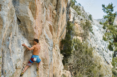 Strong man with muscular body climbing on vertical cliff with beautiful lines and stone texture, climber hiker working out outdoors with mountains view