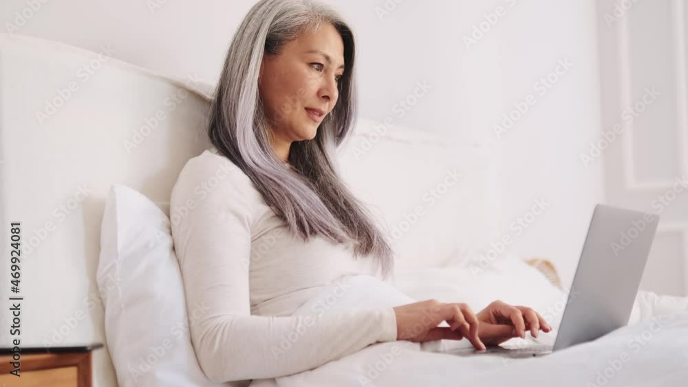 Happy Asian woman texting by laptop in the bed Happy Asian woman texting by laptop in the bed