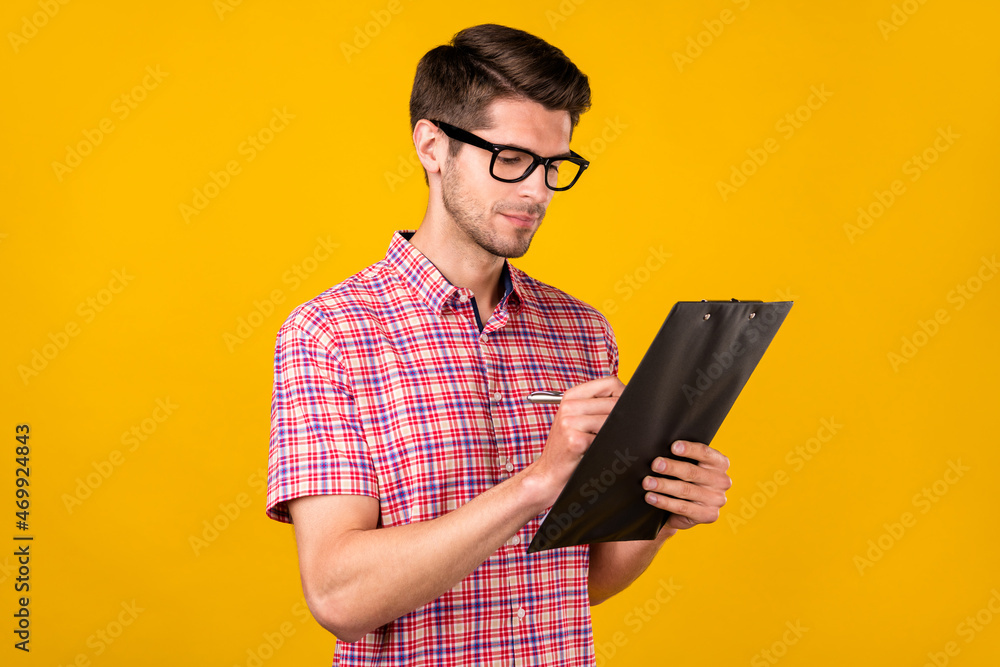 Photo of young focused serious man hold hands clip board write businessman isolated on yellow color background Photo of young focused serious man hold hands clip board write businessman isolated on yellow color background