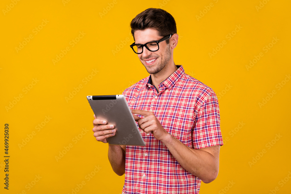 Photo of happy positive young man hold tablet smile wear glasses networking isolated on yellow color background Photo of happy positive young man hold tablet smile wear glasses networking isolated on yellow color background