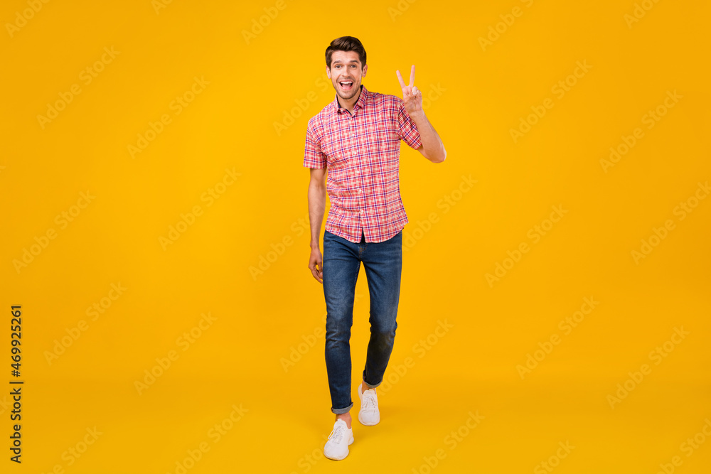 Full size photo of young man happy positive smile go walk show peace cool v-sign isolated over yellow color background Full size photo of young man happy positive smile go walk show peace cool v-sign isolated over yellow color background