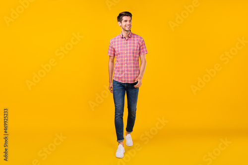 Full length photo of cheerful young happy man look empty space walk smile isolated on yellow color background