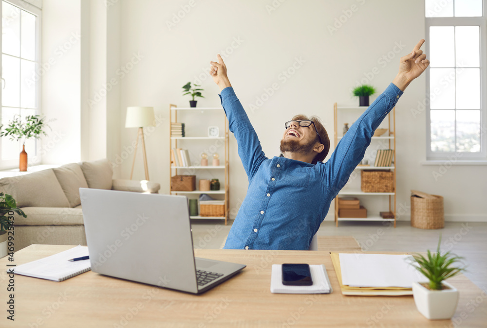 Happy young man in front of laptop computer raising hands and laughing ...