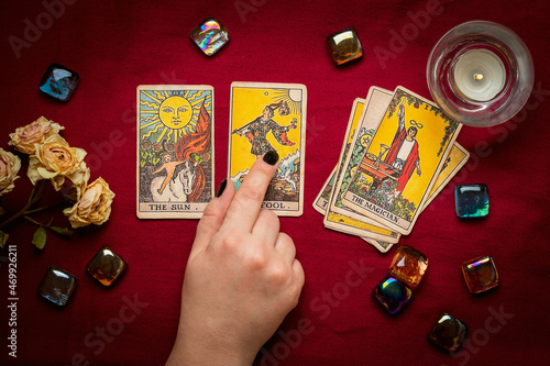 Fortuneteller's hand with black manicure lays out tarot cards, crystal, candle, dry roses on red tablecloth Flat lay Top view Fortune telling, prediction, esoteric concept