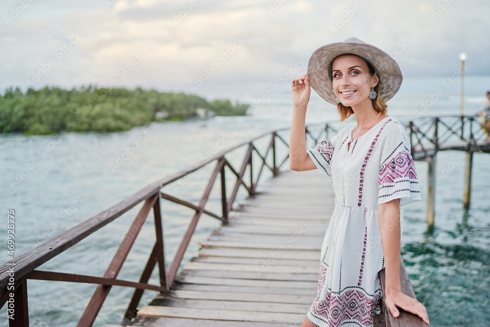 Vacation on tropical island. Young woman in hat enjoying sea view from wooden bridge terrace, Siargao Philippines.