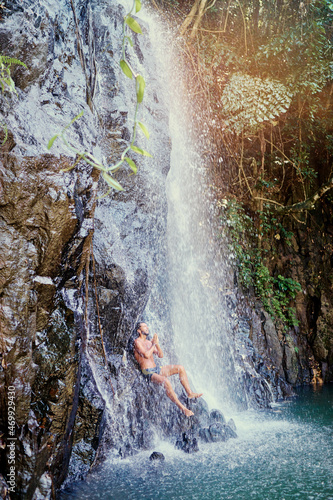 Happy young man relaxing under tropical waterfall  Vacation and relaxation.