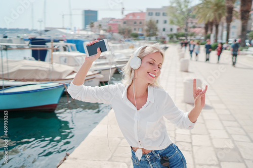 Holiday and music. Happy young woman with earphones and smartphone dancing on seafront promenade embankment. © luengo_ua