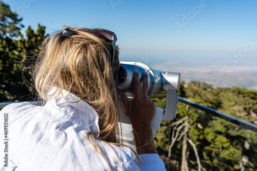 Woman looking through sightseeing binoculars (telescope) on mountains