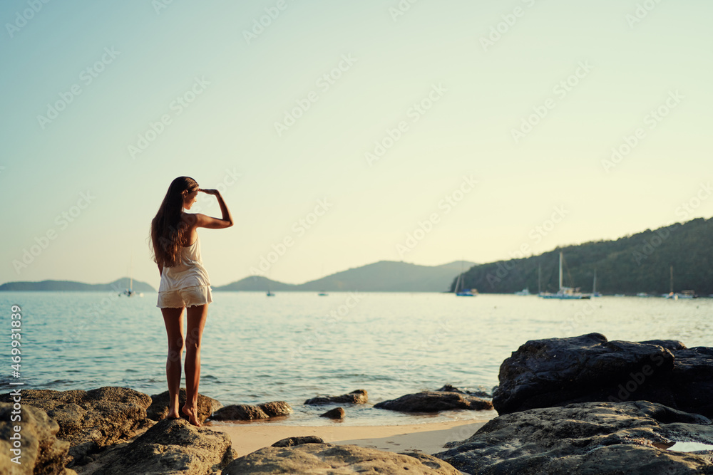 Fototapeta premium Young woman with long hear standing on sea beach enjoying the view.