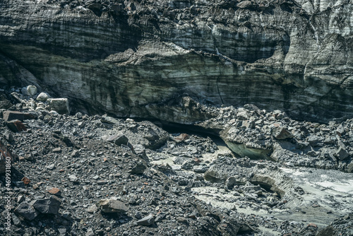 Scenic landscape with mountain river beginning from glacier among large moraines. Beautiful scenery with glacier at source of river. Mountain creek from ice among big stones. River source from glacier