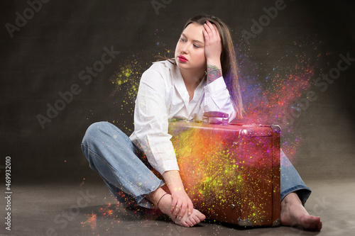 Beautiful girl sits with a vintage suitcase on a gray background.