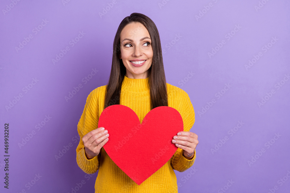 Photo of flirty brunette mature lady hold heart look empty space wear yellow sweater isolated on violet color background Photo of flirty brunette mature lady hold heart look empty space wear yellow sweater isolated on violet color background