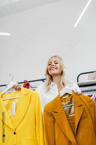 happy and blonde woman holding hangers with yellow blazers
