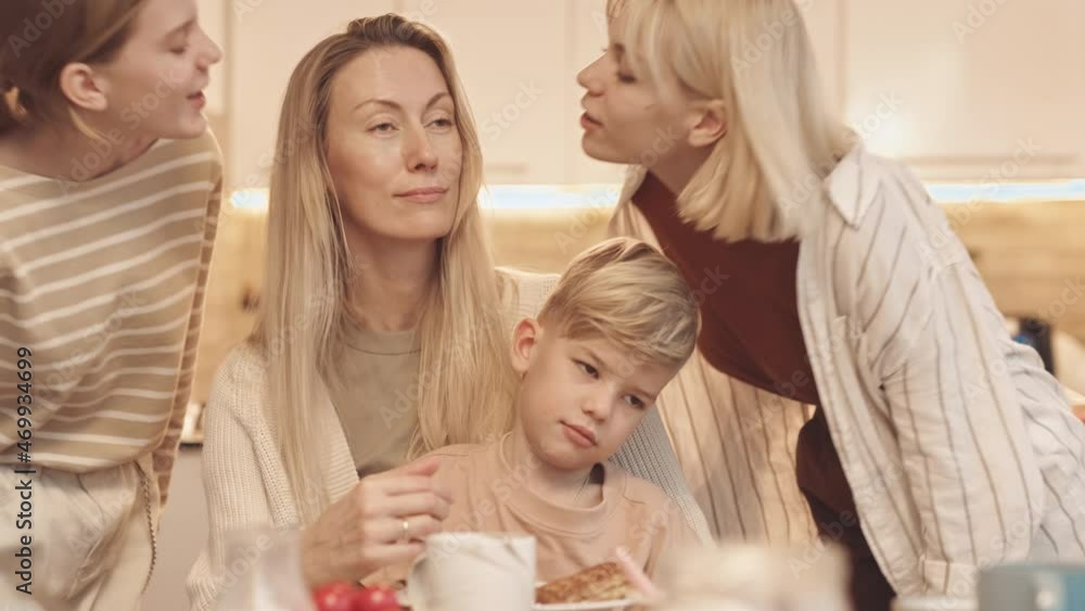 Chest-up of Caucasian woman wearing braces sitting at dining table with little son on lap, two teenage girls coming from sides and kissing mom on cheeks Chest-up of Caucasian woman wearing braces sitting at dining table with little son on lap, two teenage girls coming from sides and kissing mom on cheeks