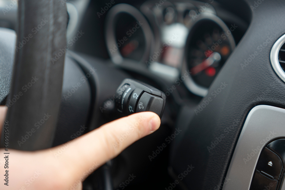 car driver hand push the button and activate windscreen wipers