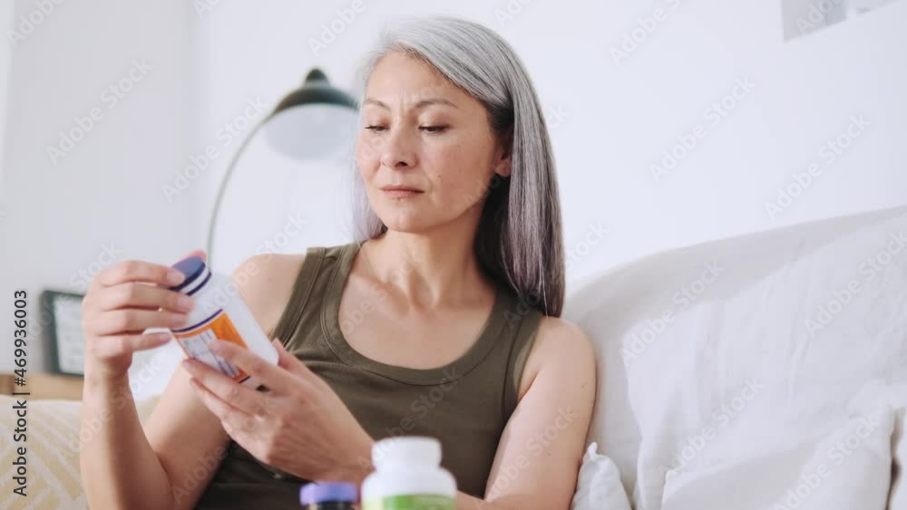 Concentrated Asian woman opening a jar of medicines at home Concentrated Asian woman opening a jar of medicines at home