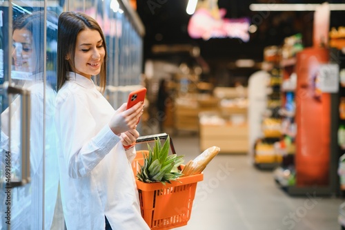 Принти на полотні Smiling young woman using mobile phone while shopping in shopping store