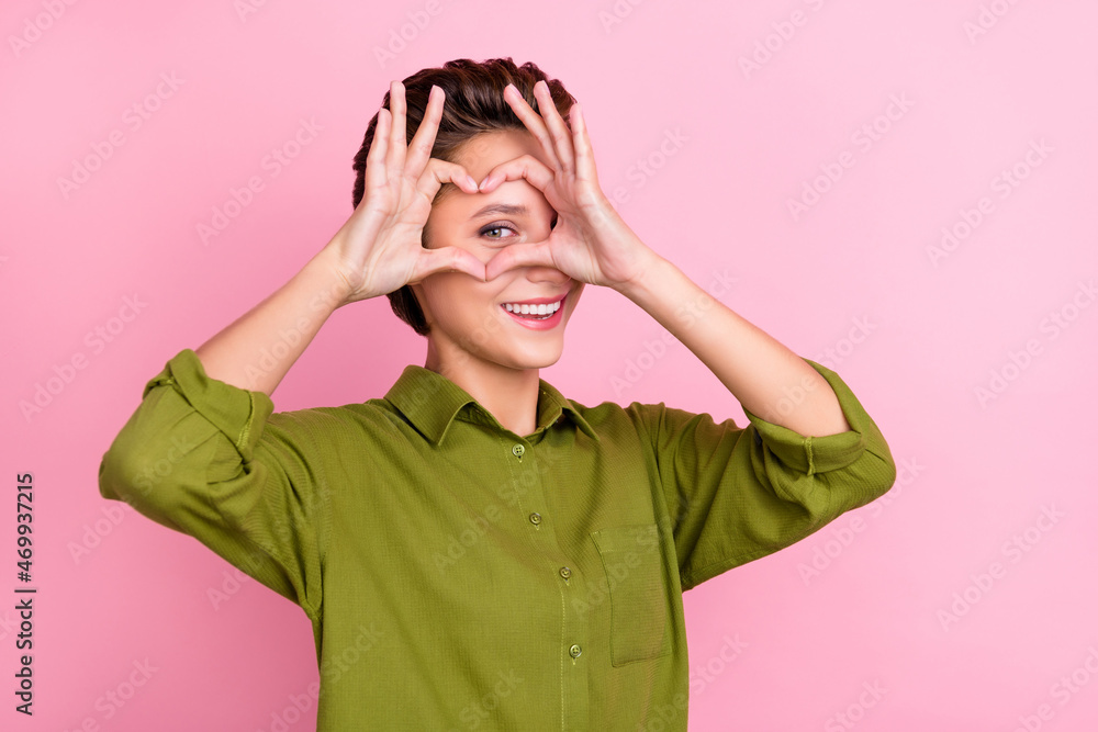 Photo of flirty playful lady fingers cover eye show heart symbol wear green shirt isolated pink color background Photo of flirty playful lady fingers cover eye show heart symbol wear green shirt isolated pink color background