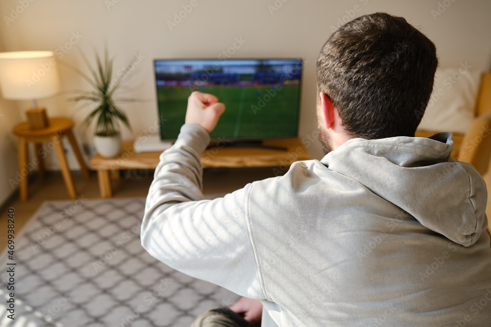 Man on the couch is watching TV. Football fan watches football and rejoices at the victory. Entertainment and sports concept. Watching sports, movies on TV at home Man on the couch is watching TV. Football fan watches football and rejoices at the victory. Entertainment and sports concept. Watching sports, movies on TV at home