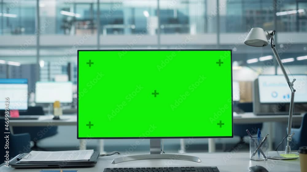 Desktop Computer Monitor with Mock Up Green Screen Chroma Key Display Standing on the Desk in the Modern Business Office. In the Background Glass Wall with Big City Office. Zoom in Shot.