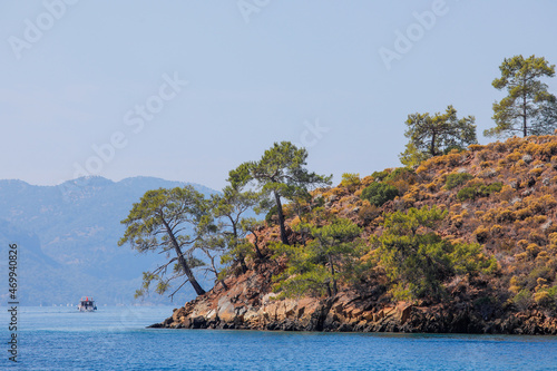 Blue sea, boat and coast with stones and trees