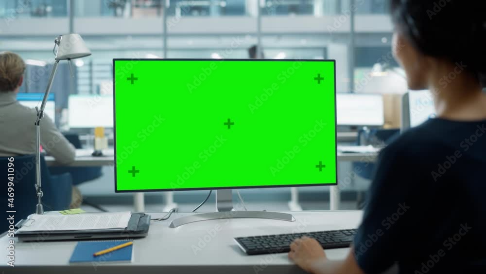 Close Up Over the Shoulder Shot of a Businesswoman Working on Desktop Computer with Chroma Key Green Screen Mock Up Display. Digital Projects Manager Typing Data, Using Keyboard and Mouse. Close Up Over the Shoulder Shot of a Businesswoman Working on Desktop Computer with Chroma Key Green Screen Mock Up Display. Digital Projects Manager Typing Data, Using Keyboard and Mouse.