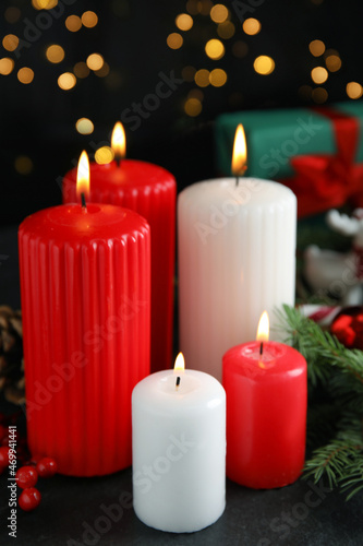 Burning candles and festive decor on dark table against blurred Christmas lights