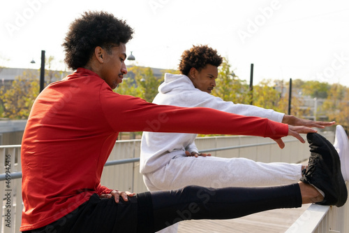 Black guy stretching hamstrings near African American friend on street