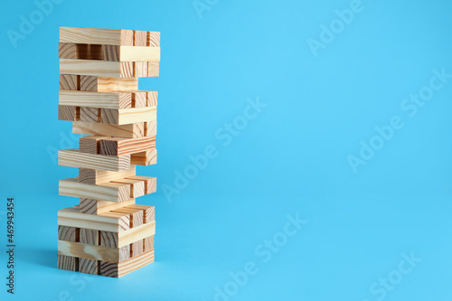 Fotografija Jenga tower made of wooden blocks on light blue background, space for text