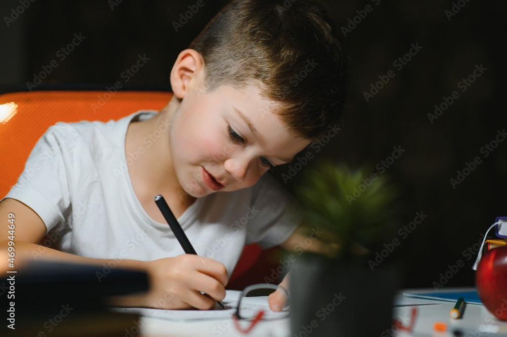 young teenager schoolboy at the table doing homework in the dark room young teenager schoolboy at the table doing homework in the dark room