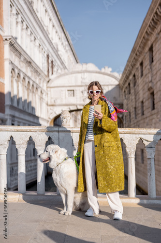 Woman enjoying great view on the Venice canal standing with her dog on the bridge. Concept of happy vacations in Venice. Idea of traveling and walking with dog. Italian style